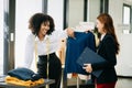 Couple of fashion designers working with fabric and clothing sketches at the studio full of tailoring tools and holds tablet and Royalty Free Stock Photo