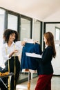 Couple of fashion designers working with fabric and clothing sketches at the studio full of tailoring tools and holds tablet and Royalty Free Stock Photo