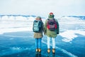 Couple of a female and male traveler with backpacks standing with their backs on frozen Baikal lake