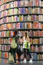 Couple of female teenagers taking selfie in front of huge bookshelf tower in international book fair