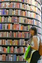 Couple of female teenagers taking selfie in front of huge bookshelf tower in international book fair