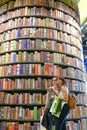 Couple of female teenagers taking selfie in front of huge bookshelf tower in international book fair