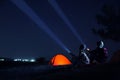 Couple with flashlights near camping tent outdoors at night