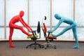 Couple in full body elastic suits exercising with chairs in office