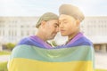 Couple of gay men in love embracing each other, wrapped in a gay flag, in a park at sunset, with reflections of the sun. Royalty Free Stock Photo