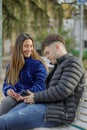 Couple of girl and boy sitting on the bench in a public park look at the mobile phone Royalty Free Stock Photo