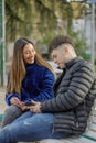 Couple of girl and boy sitting on the bench in a public park look at the mobile phone Royalty Free Stock Photo