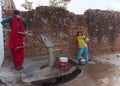 Couple girls pumping water from communal pump.