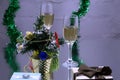 A couple of glasses with champagne on a wooden table with Christmas red balls, a glossy ribbon with a sprig of spruce on the backg