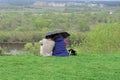 A couple of guy and girl are sitting on the green grass on the bank of the Klyazma river under one umbrella and are Royalty Free Stock Photo