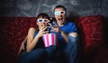 A couple of guy and girl watch a scary movie in 3D glasses and scream with fright. Popcorn.