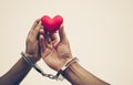 A couple` hands holding as a red heart together with hand cuffs