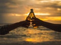 Couple hands holding beer bottles and clanging on the sunset beach. Party, Holiday, Summer, Friendship Concept. Royalty Free Stock Photo