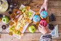 Couple of hands in top view taking two christmas sweet cakes on a wooden table with fruits and winter decorations - home party Royalty Free Stock Photo