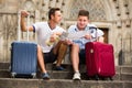 Couple of male tourists with baggage sitting with map at stairs