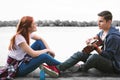 Couple of happy beaming teenagers enjoying nice evening with guitar near the river