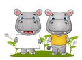 The couple of the happy hippopotamus standing and holding a blank banner in the grass field
