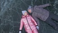 Couple has fun during winter walk against background of ice of frozen lake. Lovers lie on clear ice, have fun, kiss and Royalty Free Stock Photo