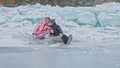 Couple has fun during winter walk against background of ice of frozen lake. Lovers lie on clear ice, have fun, kiss and Royalty Free Stock Photo