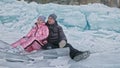 Couple has fun during winter walk against background of ice of frozen lake. Lovers lie on clear ice, have fun, kiss and Royalty Free Stock Photo