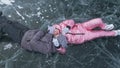 Couple has fun during winter walk against background of ice of frozen lake. Lovers lie on clear ice, have fun, kiss and Royalty Free Stock Photo