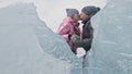 Couple has fun during winter walk against background of ice of frozen lake. Lovers lie on clear ice, have fun, kiss and Royalty Free Stock Photo