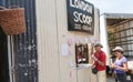 Couple in hats buying ice-cream from window opening in corrugated iron wall