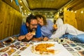Couple have fun eating pizza inside vintage hand made wooden van vehicle in alternative lifestyle and travel vacation - happy