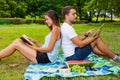 Couple having picnic. Pretty girl reads. Man is using tablet Royalty Free Stock Photo