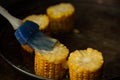 A couple of heads of golden yellow corn lie on the grill, the cook prepares corn with butter