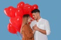 Lovely couple with heart shaped balloons on light blue background. Valentine`s day celebration Royalty Free Stock Photo