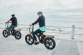 Couple, helmet or electrical bike by sea or ocean beach in bonding transport, clean energy or sustainability travel