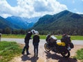 Couple in helmets are kissing. Motorcyclist adventure riders. Green meadow in Zgornje Jezersko, to Kamnik-Savinja Alps on a sunny