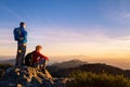 Couple of hikers with backpacks enjoying panoramic view of sunset in mountains, travel