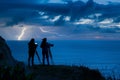 couple on hillside with camera watching lightning over ocean Royalty Free Stock Photo