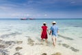 Couple holding hand walking in to crystal clear sea with long ta