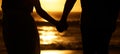 Couple holding hands on the beach at sunset. Closeup on hands of couple walking by the sea on holiday. Silhouette of Royalty Free Stock Photo