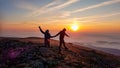 A couple holding hands and jumping on top of Babia Gora, Poland, with the panoramic view on sun rising above the horizon Royalty Free Stock Photo