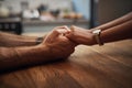 Couple holding hands in support, grief and healing together on a wooden table at home. Closeup of a caring partner in