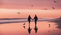 A couple holding hands and walking on a beach at sunset. The sky is orange and pink, and the ocean is calm. There Royalty Free Stock Photo