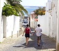 Couple holding hands walking down picturesque street of Lagos, Portugal.