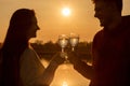 A couple holds glasses with drinks against the backdrop of a sunny sunset