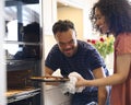 Couple At Home With Man With Down Syndrome And Woman Taking Pizza Out Of Oven In Kitchen Royalty Free Stock Photo