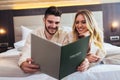 Couple in hotel room reading room service menu together in bed Royalty Free Stock Photo