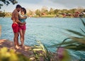 Couple hugging. Young man and woman in embrace, standing by water on wooden jetty. Blue water and houses in background. Royalty Free Stock Photo