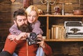 Couple hugs in wooden vintage interior. Man with beard, photographer on busy face holds old fashioned camera. Couple in