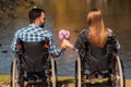 A couple of invalids on wheelchairs met in the park. A man and a woman are holding a bouquet of flowers.