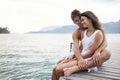 Couple, jetty and hug by ocean on vacation, love and relax by water on summer holiday. People, embrace and bonding for