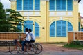 Couple Khmer teens riding bicycle pass old french colonial building. Scenic landscape town of Kampot, South Cambodia Royalty Free Stock Photo