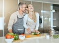 Couple in kitchen cooking together in their home, having fun and laughing. Middle aged man and woman cutting healthy